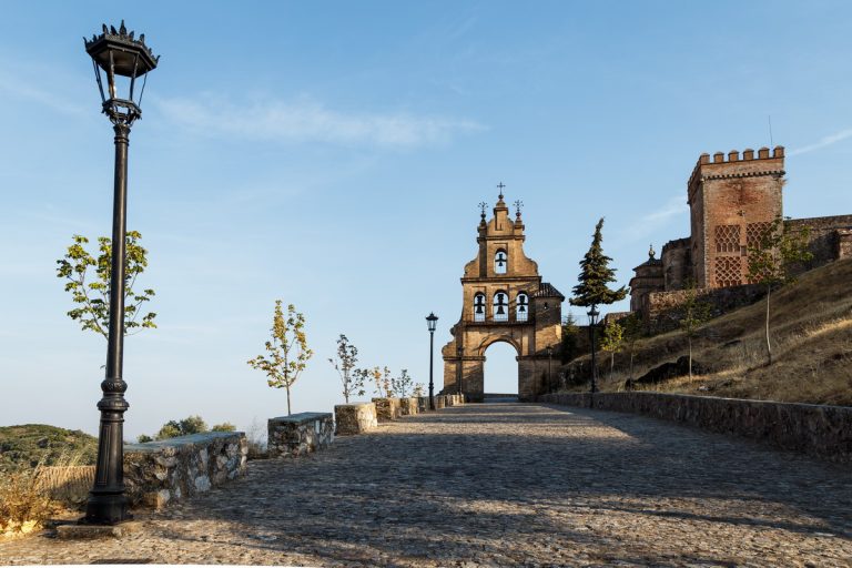 A beautiful view of an alley leading to the big arc with black bells on it and a castle